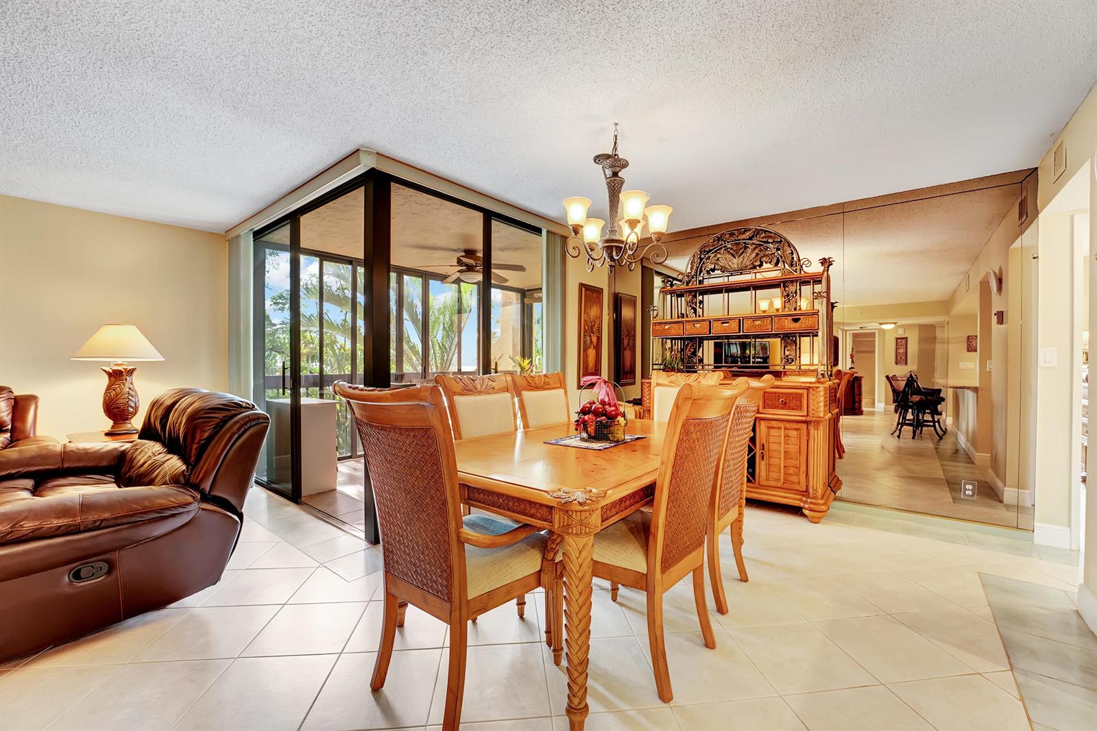 A dining room with a wooden table and chairs sits beside a glass-enclosed balcony — 450 Egret Circle # 9202, Delray Beach FL 33444, DELRAY BEACH, FL