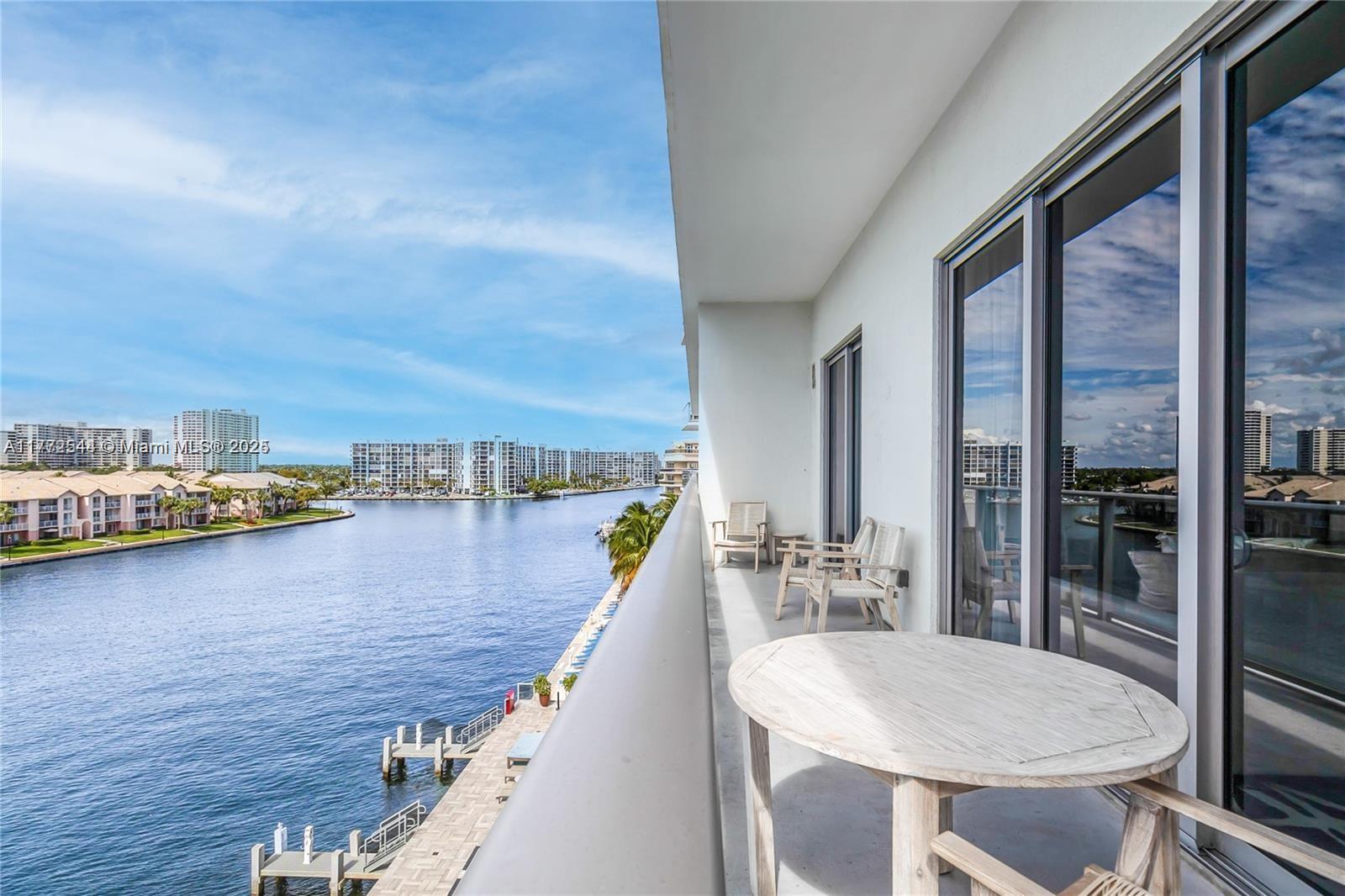 A balcony with a round wooden table and chairs overlooks a canal and apartment buildings — 4010 S Ocean Dr # R406, Hollywood FL 33019, HOLLYWOOD, FL