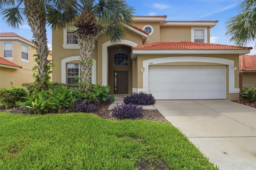 A two-story tan house with a tile roof, a two-car garage, and palm trees — 165 SEVILLA AVENUE, DAVENPORT, FL