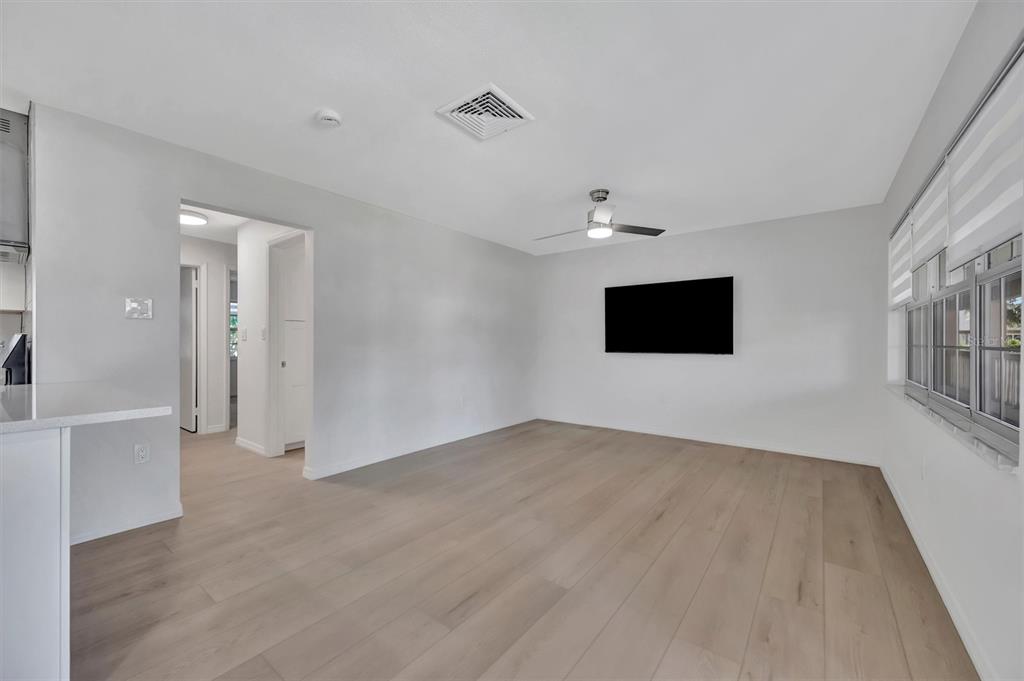 A bright living room features light wood-look flooring, white walls, a ceiling fan, and a television — 650 PINELLAS POINT DRIVE S UNIT 216, ST PETERSBURG, FL
