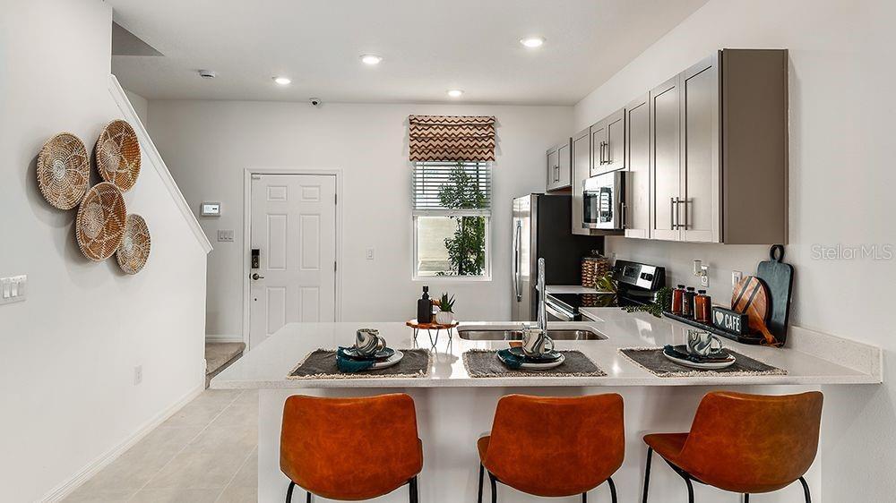 A modern kitchen features a white island with three orange chairs and gray cabinets — 10637 ORBIT TERRACE, SARASOTA, FL