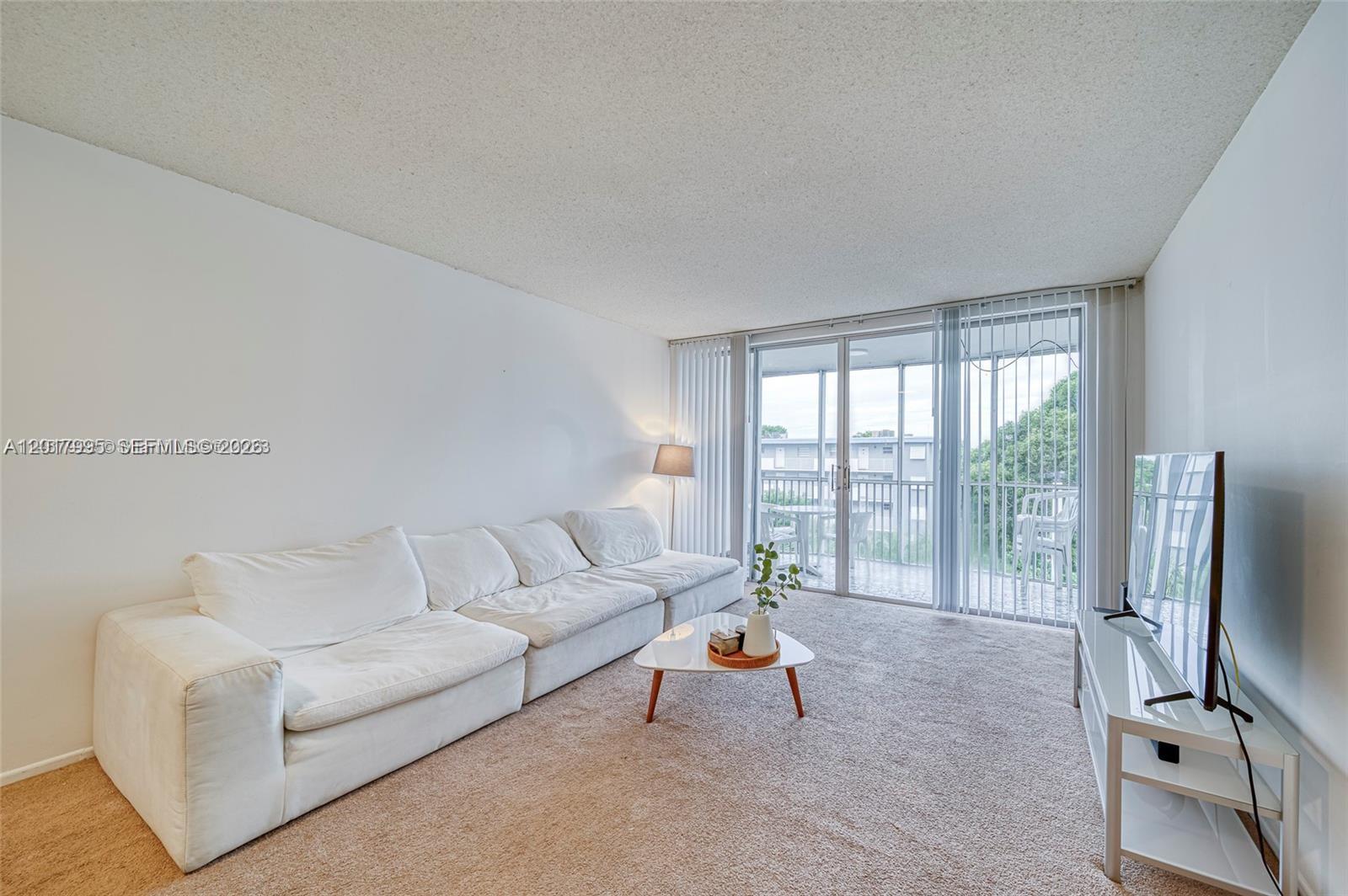 A living room features a white sectional sofa, a coffee table, and a balcony view — 1690 NE 191st St # 1, Miami FL 33179, MIAMI, FL