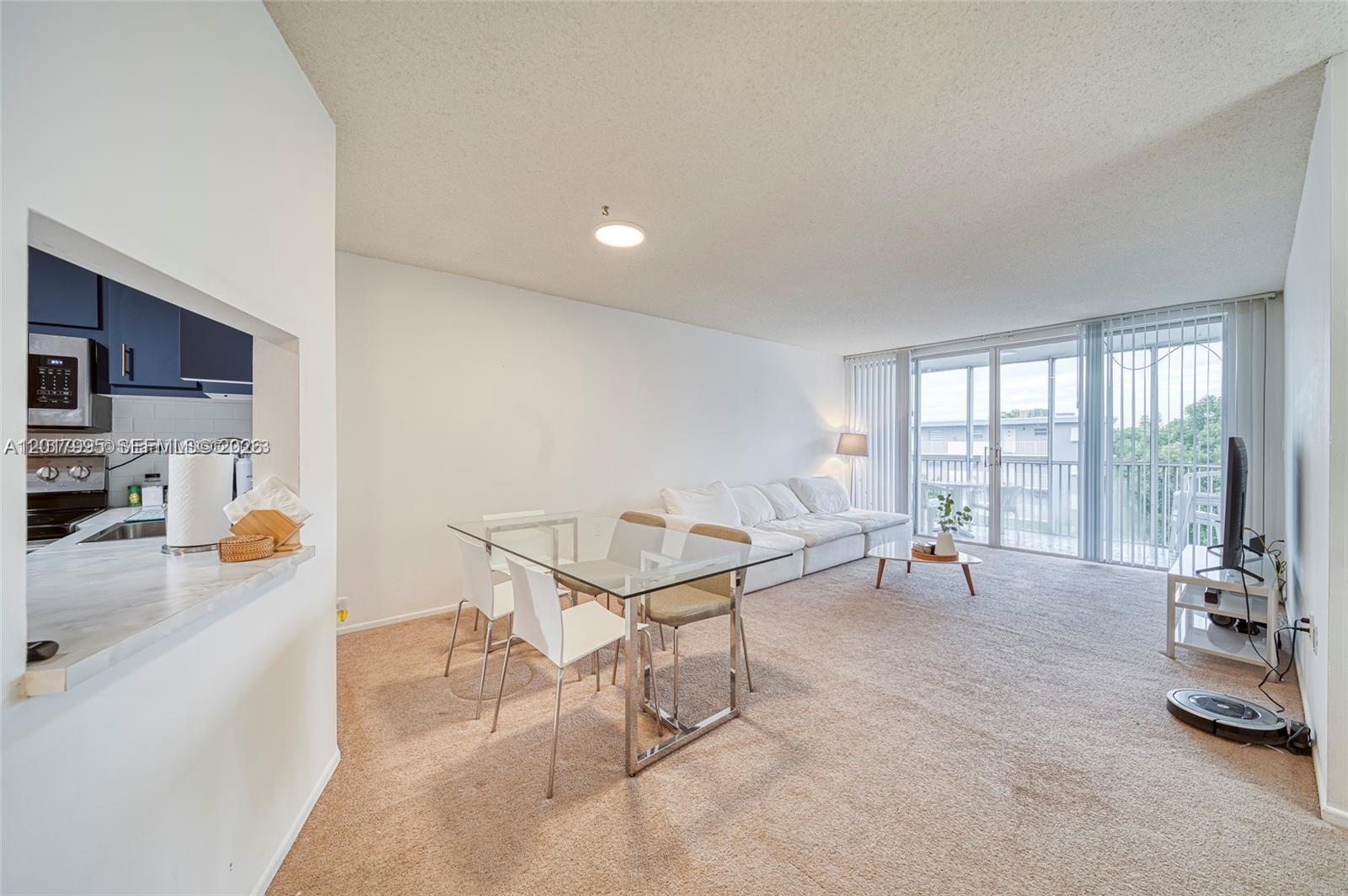 A living and dining area features beige carpeting, a glass table, and a sliding balcony door — 1690 NE 191st St # 1, Miami FL 33179, MIAMI, FL