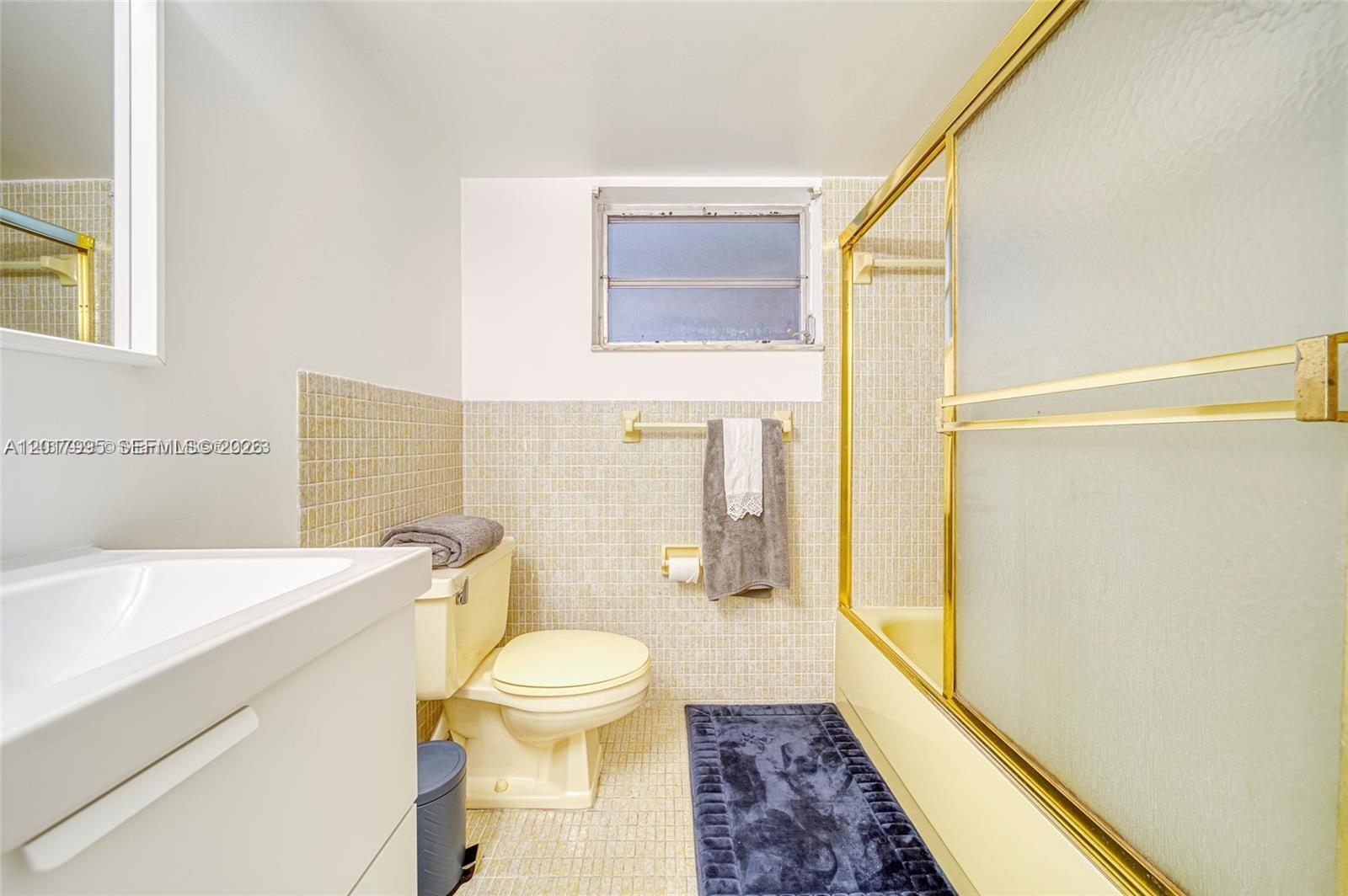 A bathroom features a yellow bathtub, a matching toilet, and gold-framed shower doors — 1690 NE 191st St # 1, Miami FL 33179, MIAMI, FL