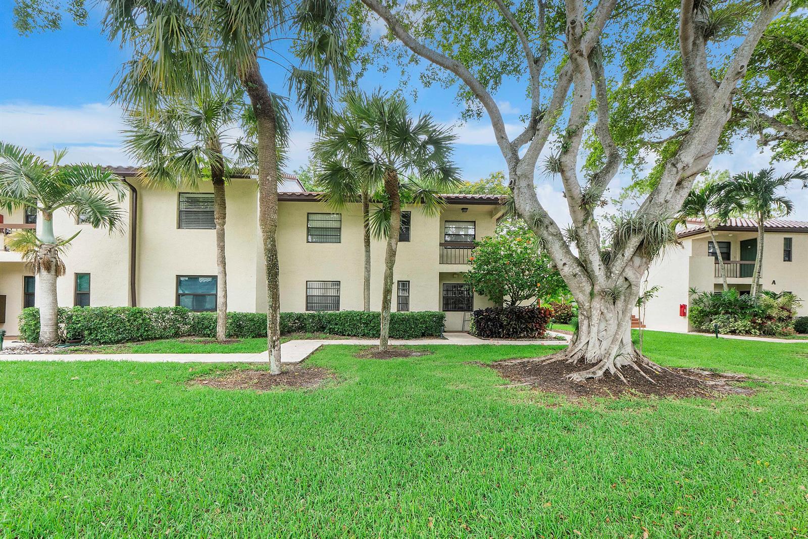 A two-story apartment building exterior with palm trees, a large tree, and a grassy lawn — 21852 Arriba # h, Boca Raton FL 33433, BOCA RATON, FL