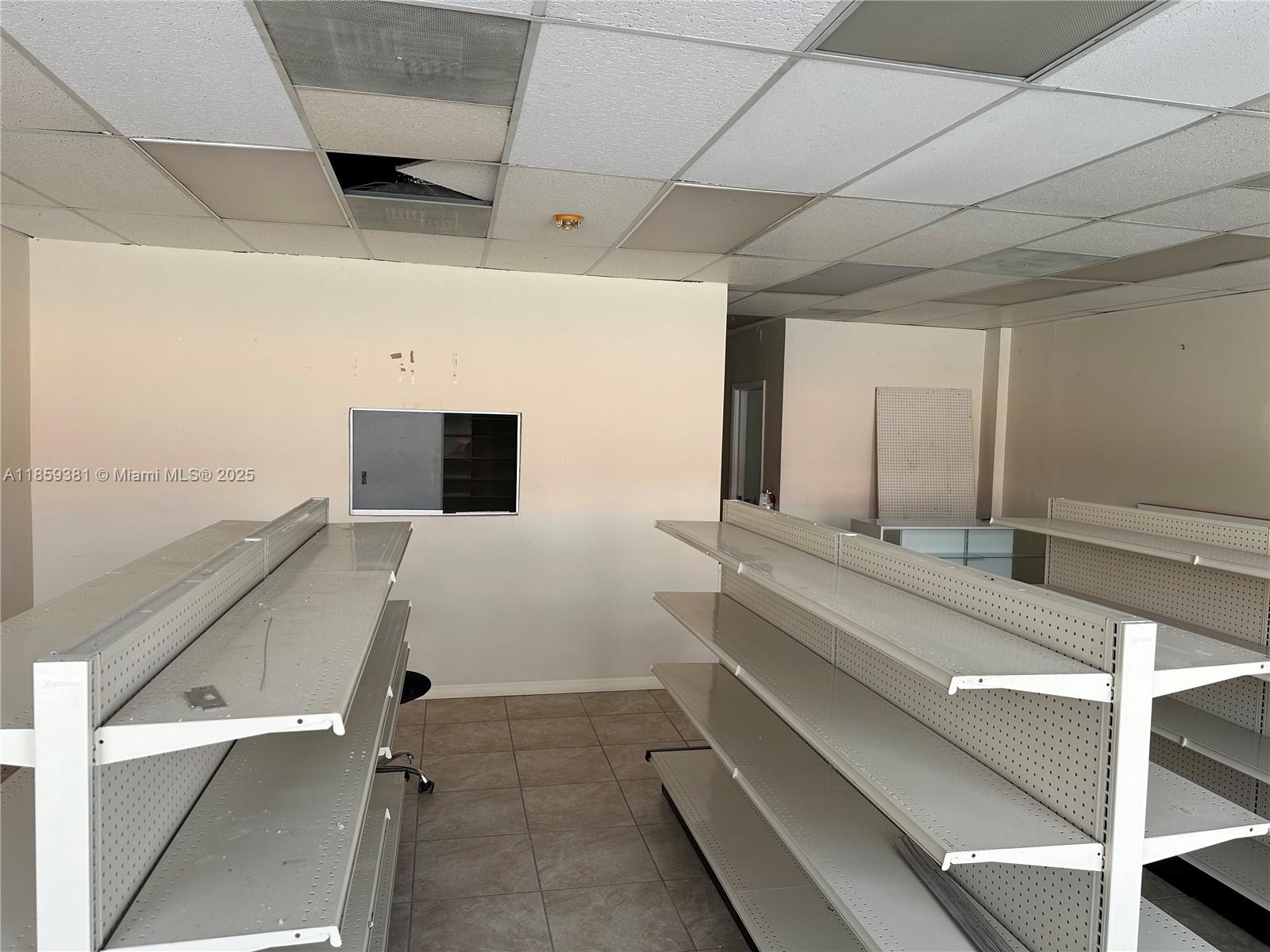 An empty retail space features metal shelving units, tiled floors, and a damaged drop ceiling — 455 SW 17th Ave, Miami FL 33135, MIAMI, FL