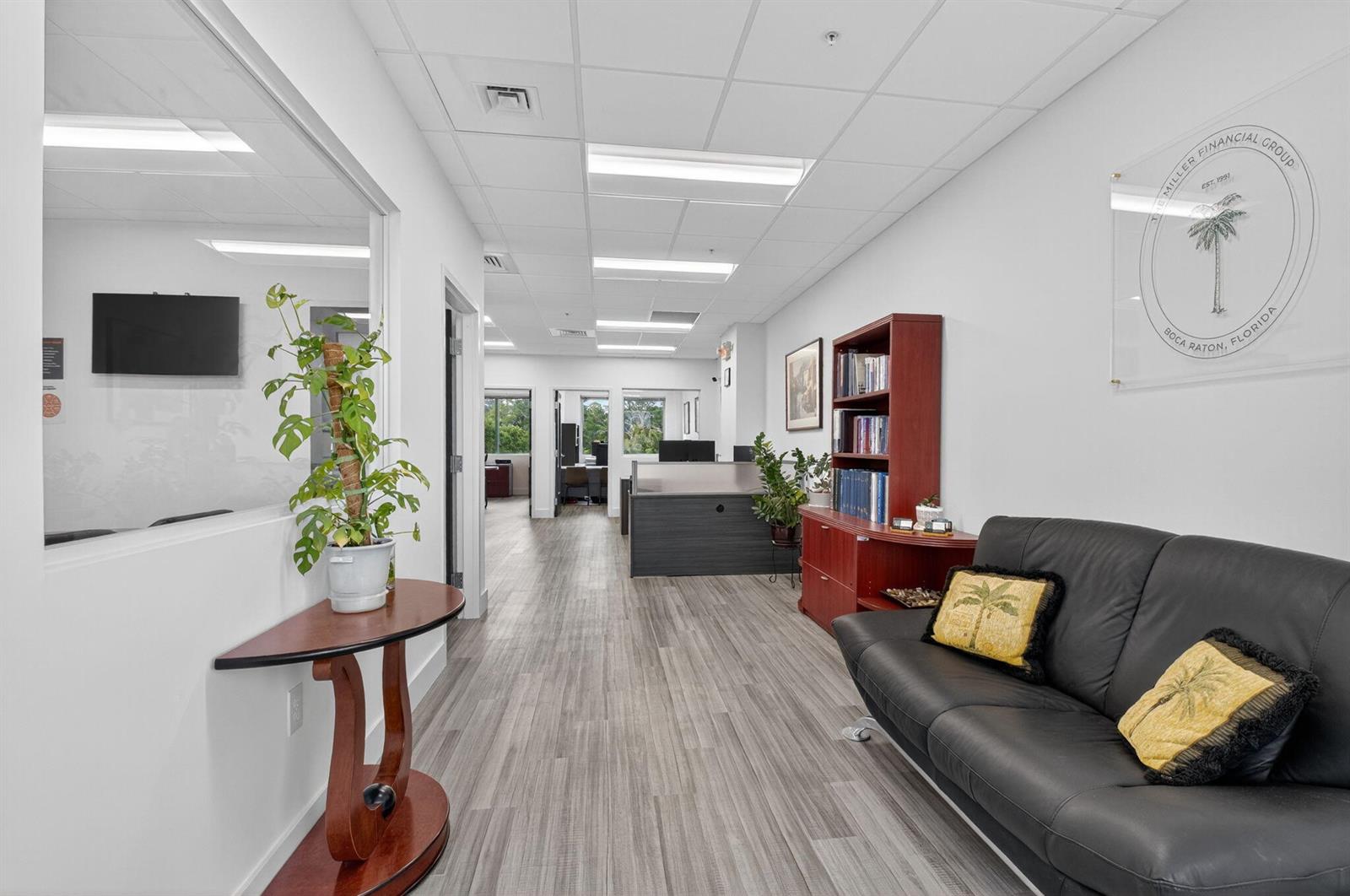 An office hallway features a black leather sofa, a wooden bookshelf, and a glass-walled room — 7700 Congress Avenue # 3211, Boca Raton FL 33487, BOCA RATON, FL