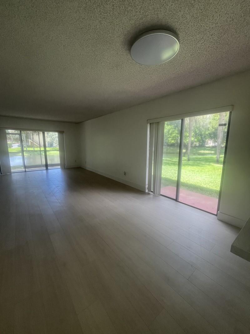 An empty living room features light wood-look flooring, a popcorn ceiling, and two sliding glass doors — 235 Lakeview Drive # 104, Weston FL 33326, WESTON, FL