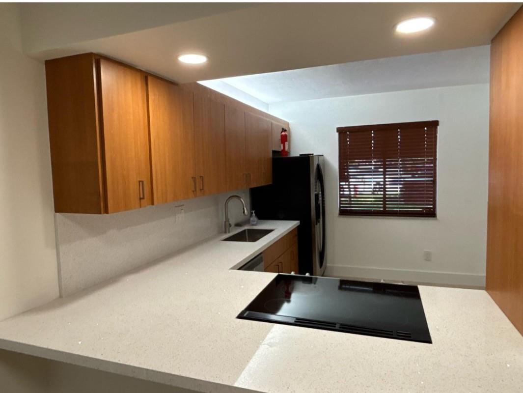 A kitchen features wood cabinets, white countertops, a black cooktop, and a stainless steel sink — 235 Lakeview Drive # 104, Weston FL 33326, WESTON, FL