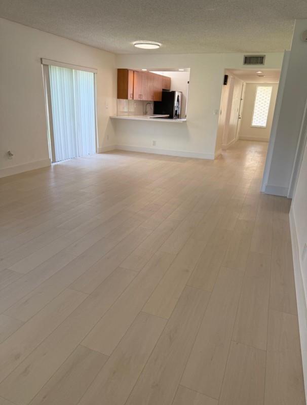 An open-concept living area features light-colored wood flooring, a pass-through kitchen, and sliding glass doors — 235 Lakeview Drive # 104, Weston FL 33326, WESTON, FL