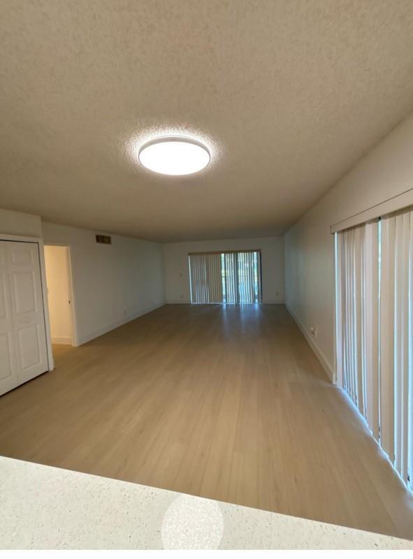 An empty living room with light wood-look flooring, a ceiling light, and vertical window blinds — 235 Lakeview Drive # 104, Weston FL 33326, WESTON, FL
