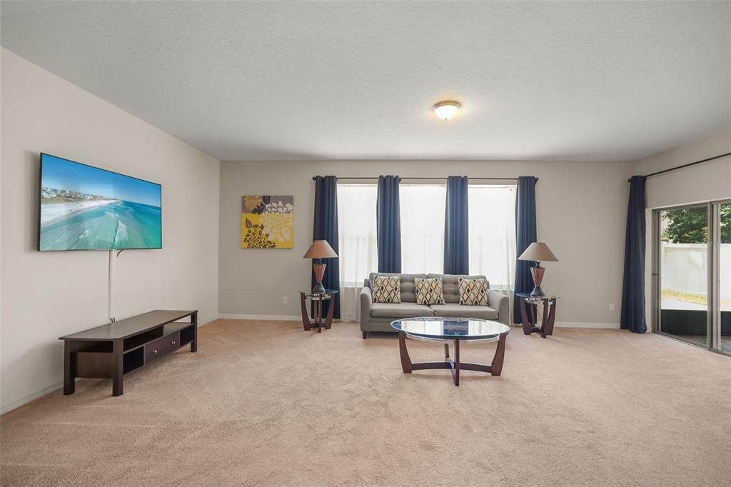 A living room features beige carpeting, a mounted television, a sofa, and sliding glass doors — 1612 PINE MARSH LOOP, ST CLOUD, FL