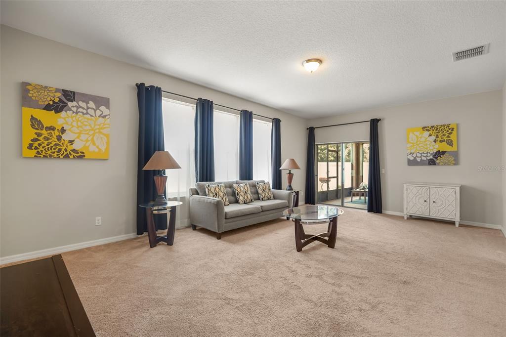 A living room features a gray sofa, glass coffee table, and yellow floral wall art — 1612 PINE MARSH LOOP, ST CLOUD, FL