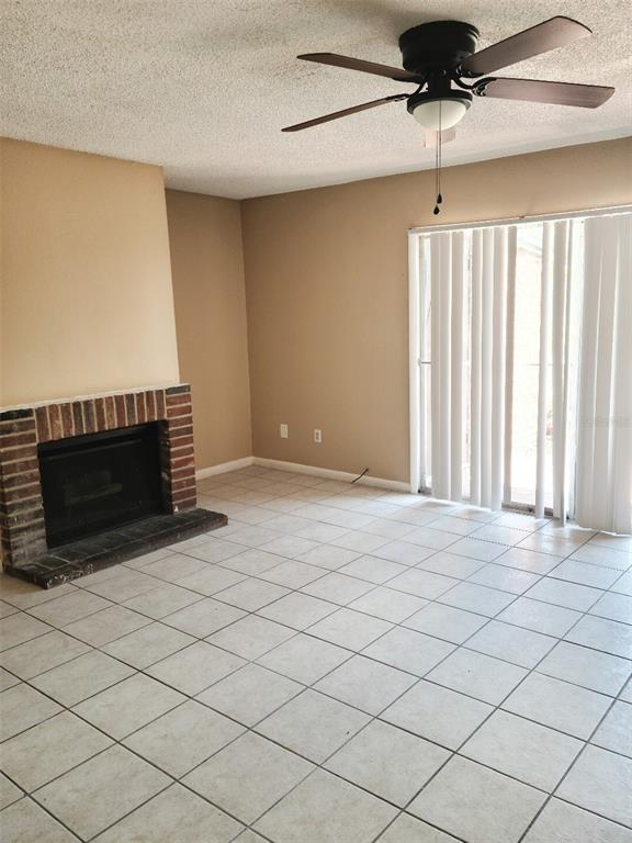 A living room features a brick fireplace, tile flooring, a ceiling fan, and sliding doors — 2330 HUNTINGTON GREEN CT UNIT 6, ORLANDO, FL
