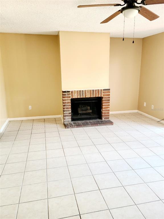 A room with light-colored tile flooring, beige walls, and a brick fireplace — 2330 HUNTINGTON GREEN CT UNIT 6, ORLANDO, FL
