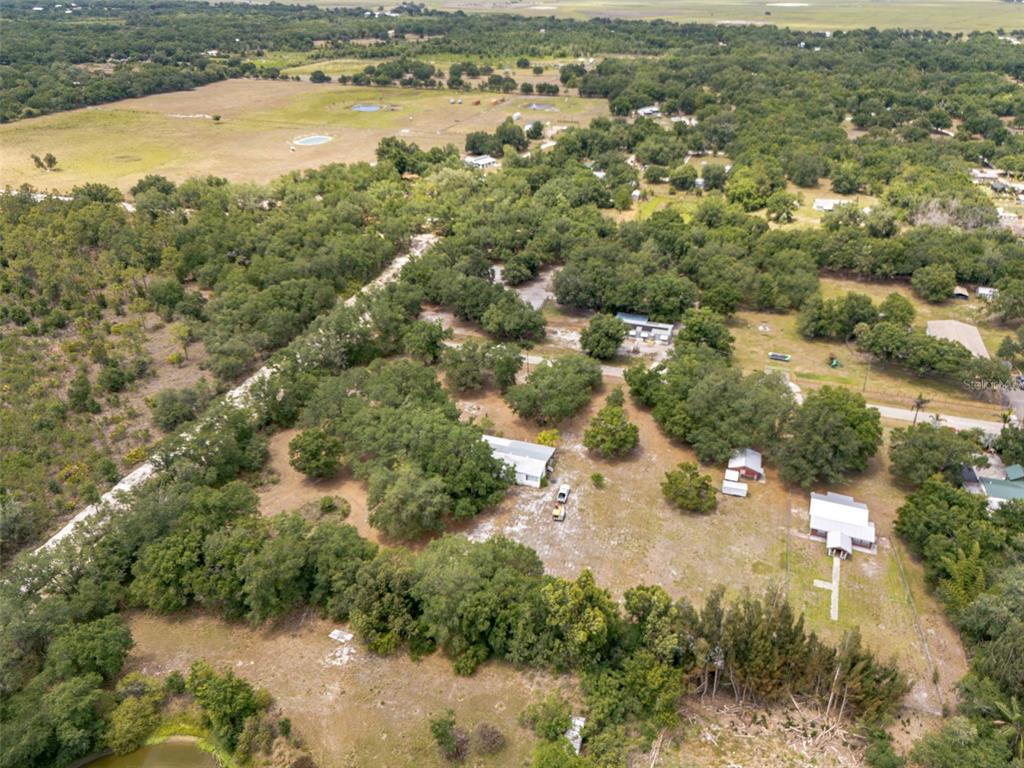 An aerial view shows a rural property with a house, outbuildings, and surrounding wooded land — 4981 NW HICKORY STREET, ARCADIA, FL