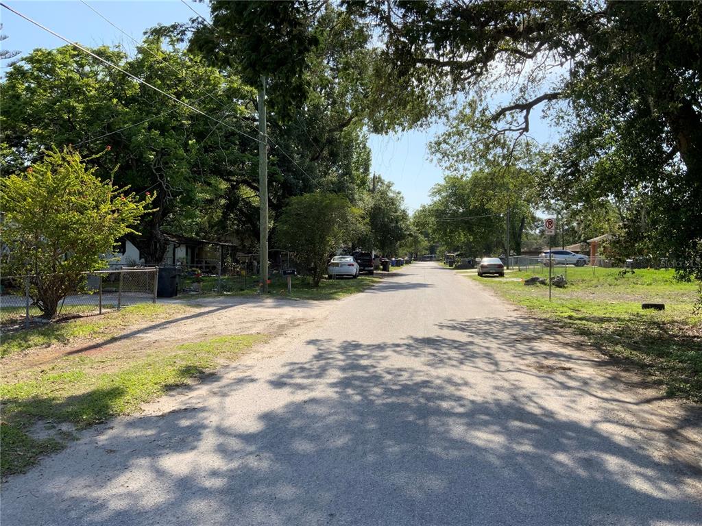 A paved residential street lined with trees, parked cars, and houses on a sunny day — 5902 N 50TH STREET, TAMPA, FL