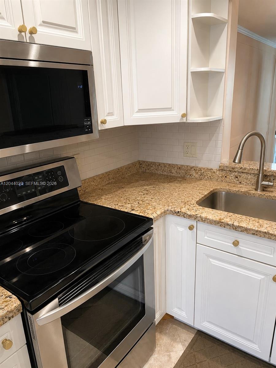 A kitchen features white cabinets, a stainless steel microwave and stove, and granite countertops — 219 NE 14th Ave # 306, Hallandale Beach FL 33009, HALLANDALE BEACH, FL