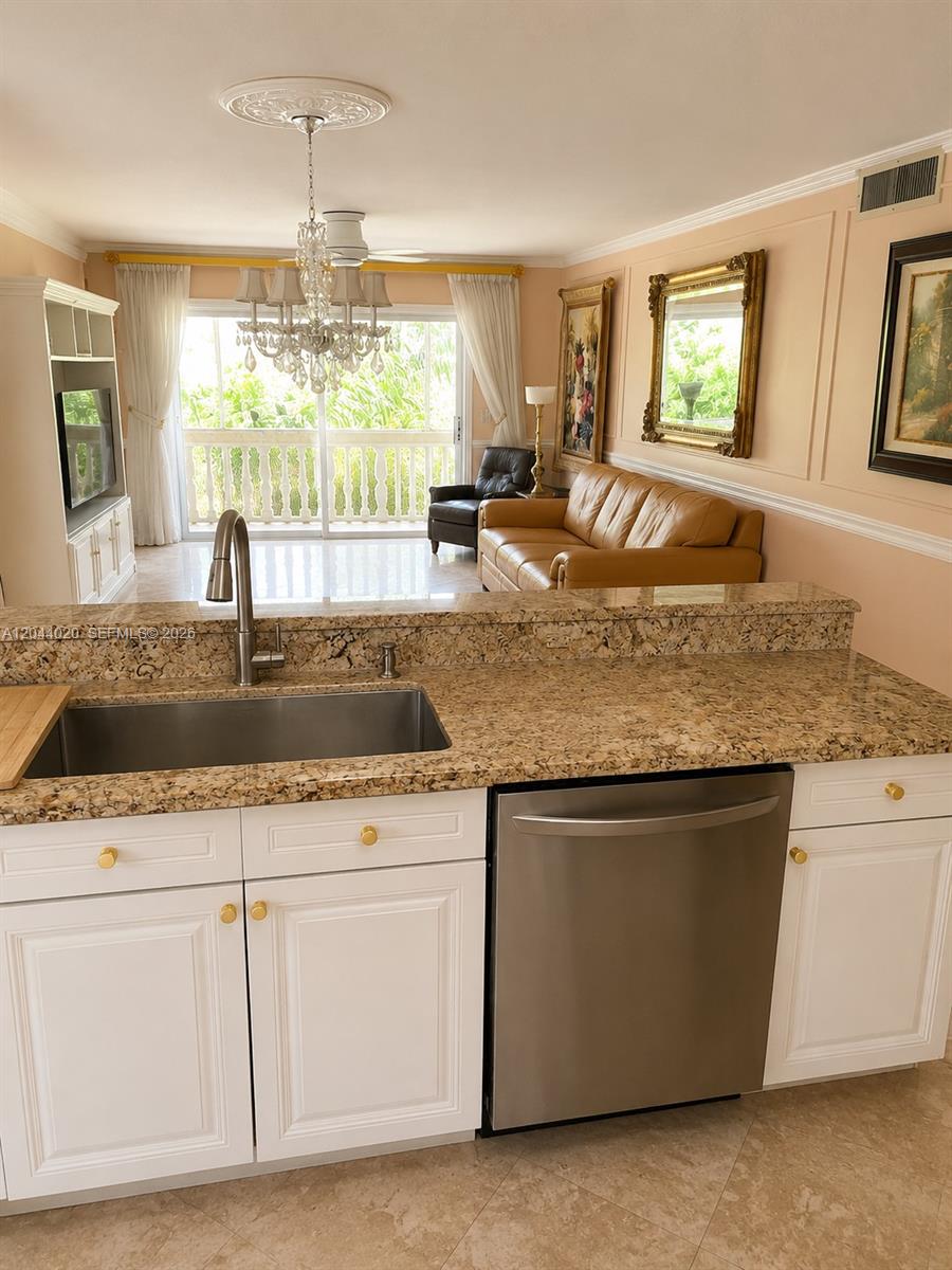 A kitchen with granite countertops and white cabinets overlooks a living room with a balcony — 219 NE 14th Ave # 306, Hallandale Beach FL 33009, HALLANDALE BEACH, FL