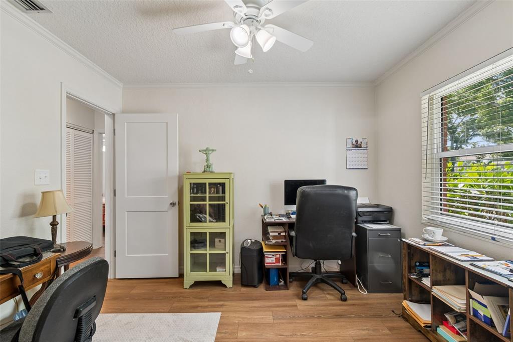 A home office features wood-look flooring, a ceiling fan, a desk, and a storage cabinet — 4727 W ANITA BOULEVARD, TAMPA, FL