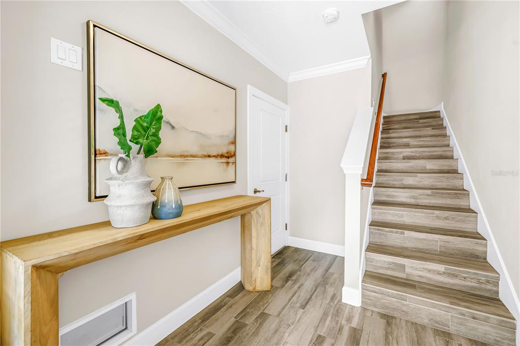 A foyer features a wooden console table, wall art, and stairs with wood-look tile flooring — 3207 NAUTICAL PLACE S, ST PETERSBURG, FL