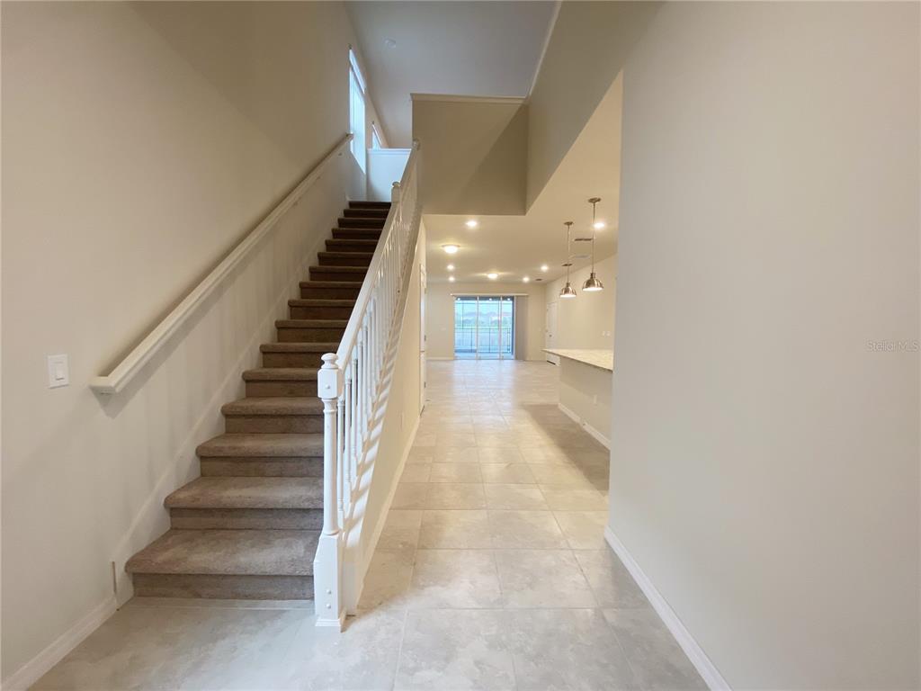 A carpeted staircase with a white railing leads to an open-concept living area with tile — 7360 OAKMOSS LOOP, DAVENPORT, FL