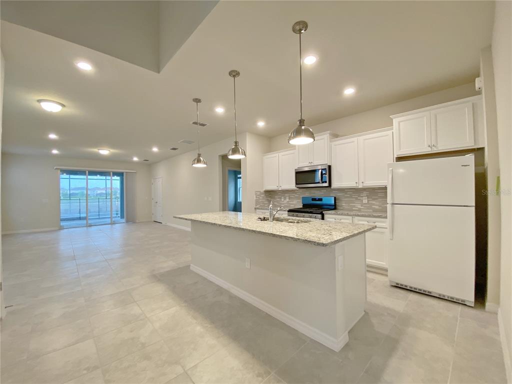 A kitchen with a granite island, white cabinets, and stainless steel appliances opens to a living area — 7360 OAKMOSS LOOP, DAVENPORT, FL