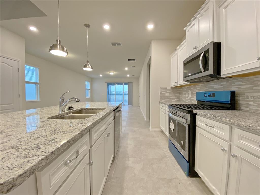 A kitchen features white cabinets, granite countertops, stainless steel appliances, and a large island — 7360 OAKMOSS LOOP, DAVENPORT, FL