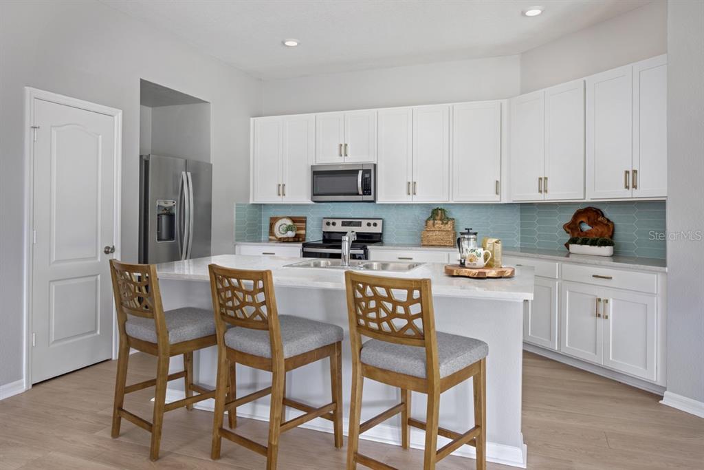A kitchen features white cabinets, a light-colored island with bar stools, and blue backsplash tile — 5531 CREEK HAVEN WAY, LAKELAND, FL