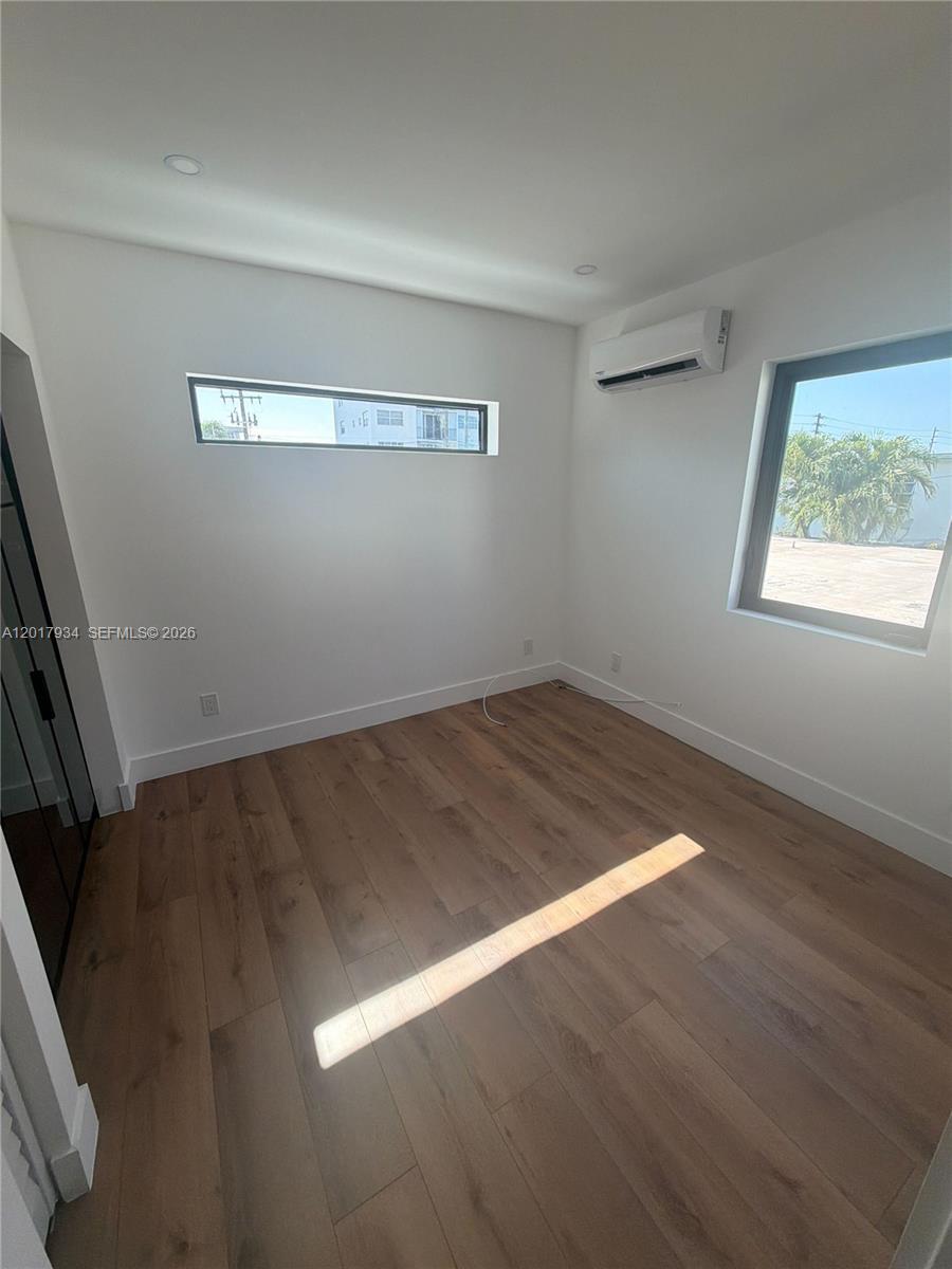 An empty room features light wood-look flooring, white walls, a mini-split unit, and two windows — 7801 Byron Ave # 3, Miami Beach FL 33141, MIAMI BEACH, FL
