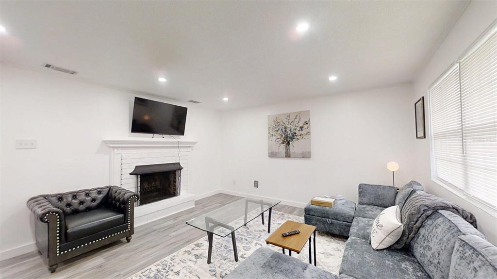A living room features a fireplace with a mounted television, gray flooring, and sectional seating — 1335 NE 10TH STREET, OCALA, FL