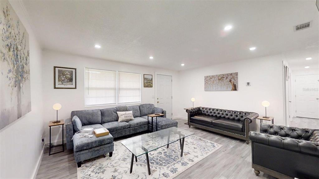 A living room features gray flooring, a blue sectional, a black leather sofa, and artwork — 1335 NE 10TH STREET, OCALA, FL