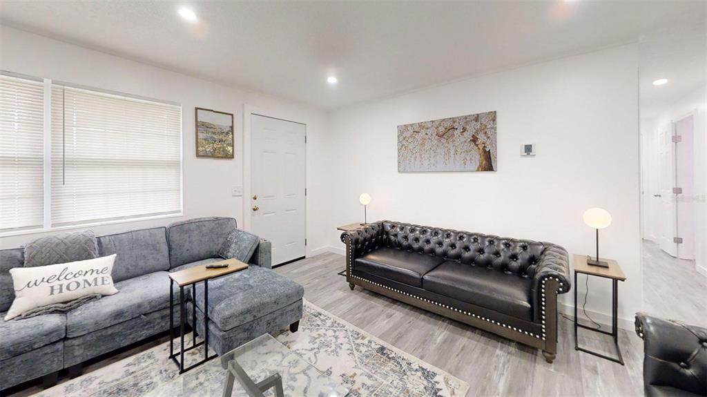 A living room features a grey sectional, a black tufted sofa, and light wood flooring — 1335 NE 10TH STREET, OCALA, FL