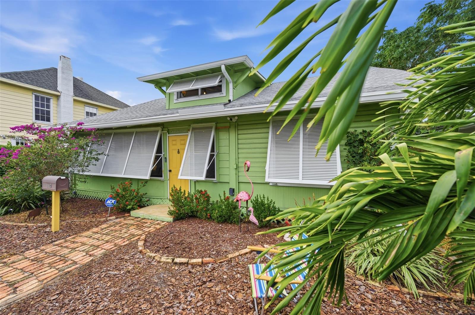 A lime green house with a yellow door and white shutters sits behind a brick walkway — 117 S Palmway, FL 33460, FL