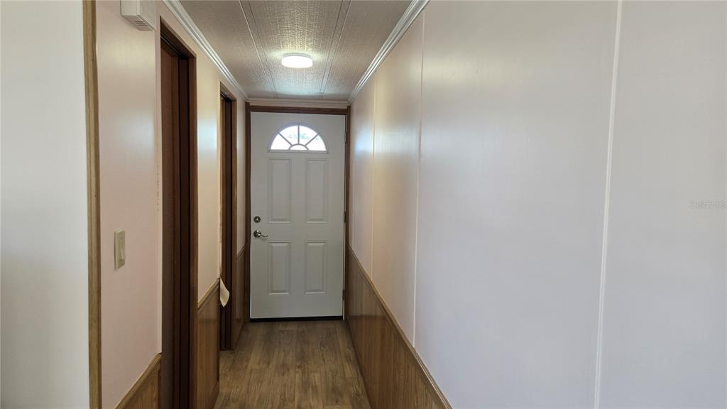 A hallway with wood-paneled wainscoting, white walls, and a white exterior door at the end — 3333 26TH AVENUE E UNIT 1291, BRADENTON, FL