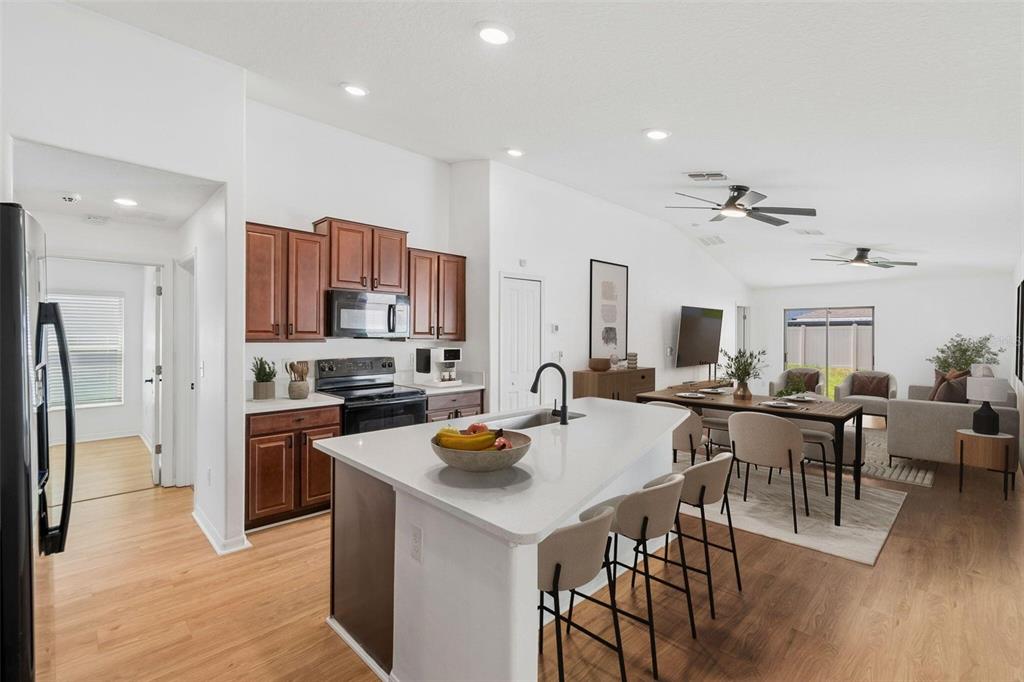 An open-concept kitchen with a white island and wooden cabinets overlooks a dining and living area — 7227 SALT RIVER, SUN CITY CENTER, FL