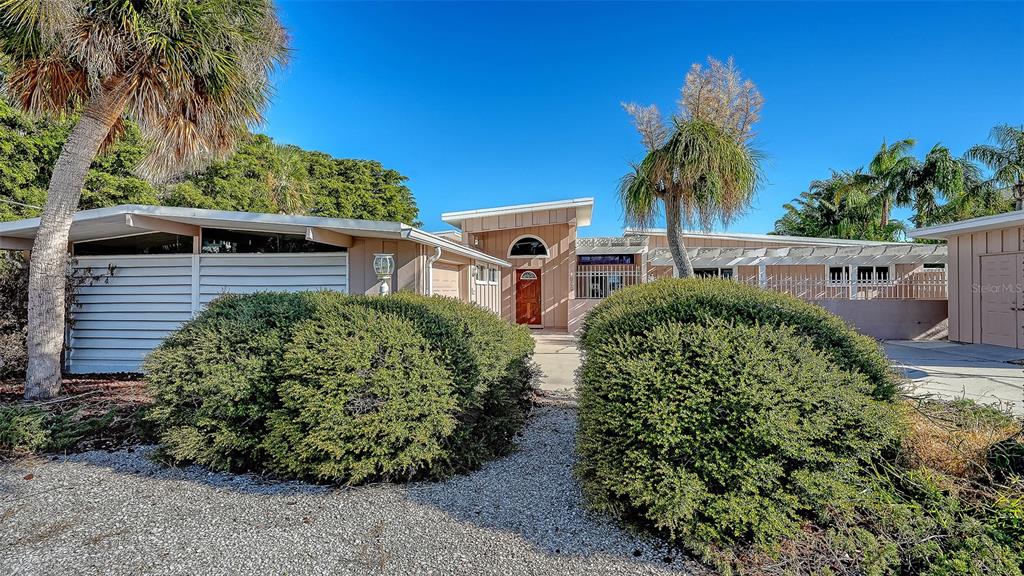A single-story house with a flat roof, light wood siding, and two large rounded bushes — 355 S SHORE DRIVE, SARASOTA, FL