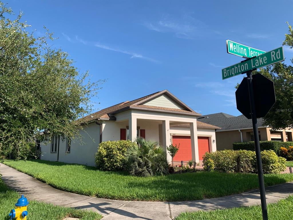 A single-story house with a tan exterior and orange garage doors sits on a corner lot — 4063 WELLING TERRACE, LAND O LAKES, FL