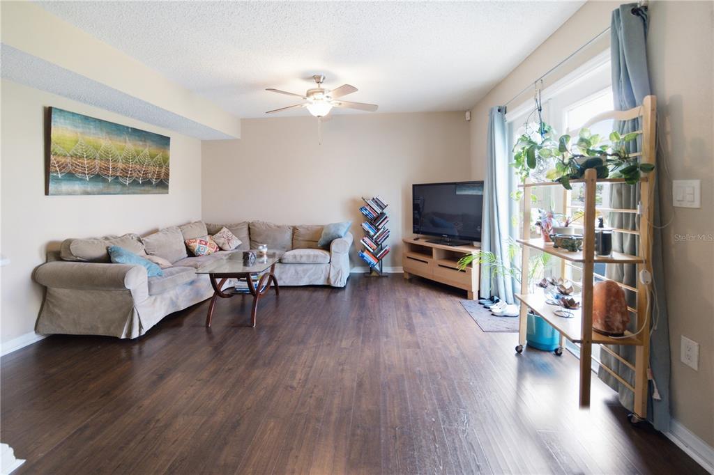 A living room features a sectional sofa, a television on a stand, and wood flooring — 12414 TOUCHTON DRIVE UNIT 100, TAMPA, FL