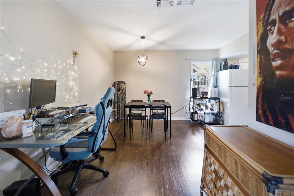 A dining area with a desk, gaming chair, and kitchen appliances on dark wood flooring — 12414 TOUCHTON DRIVE UNIT 100, TAMPA, FL