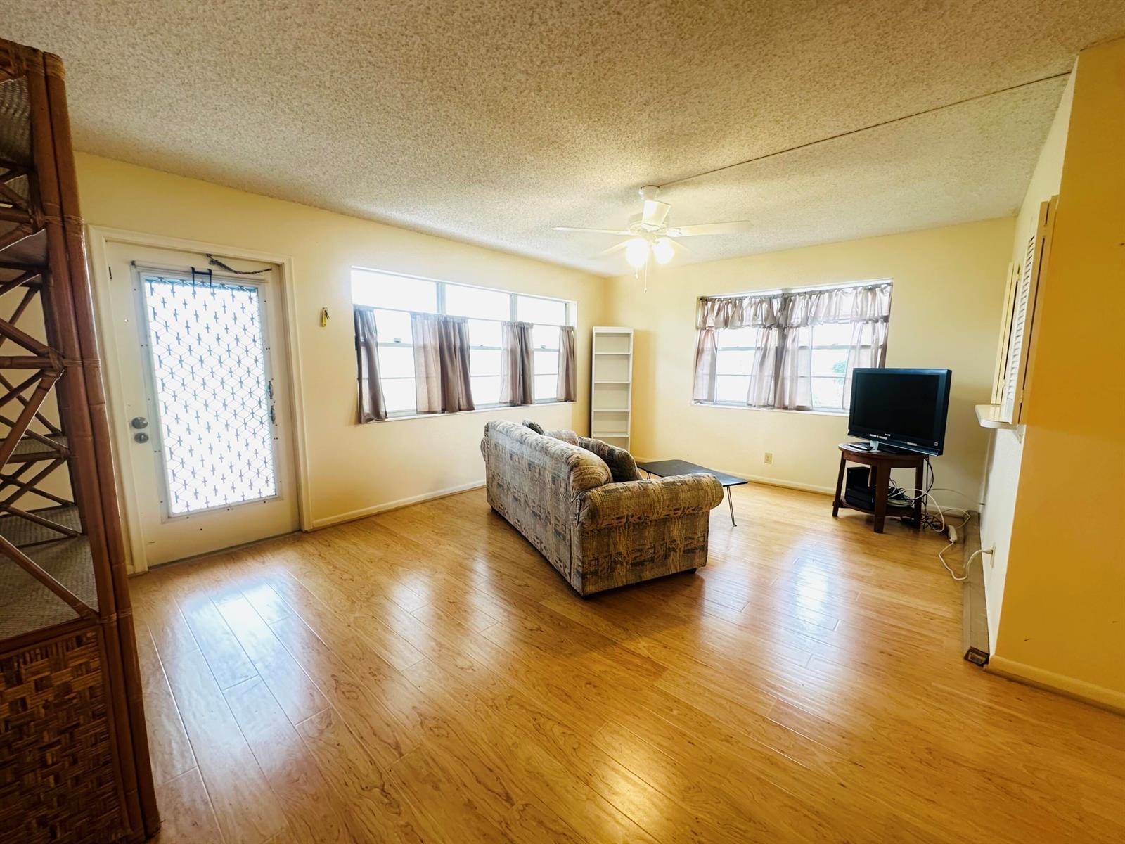 A living room with light wood flooring, a patterned sofa, and two windows with curtains — 269 Farnham L, Deerfield Beach FL 33442, DEERFIELD BEACH, FL