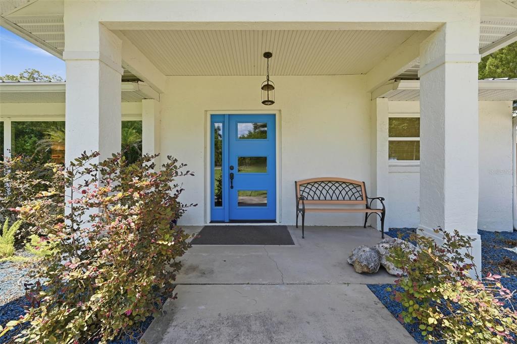 A covered front porch features a bright blue door, a metal bench, and landscaping — 37237 GRAYS AIRPORT ROAD, LADY LAKE, FL