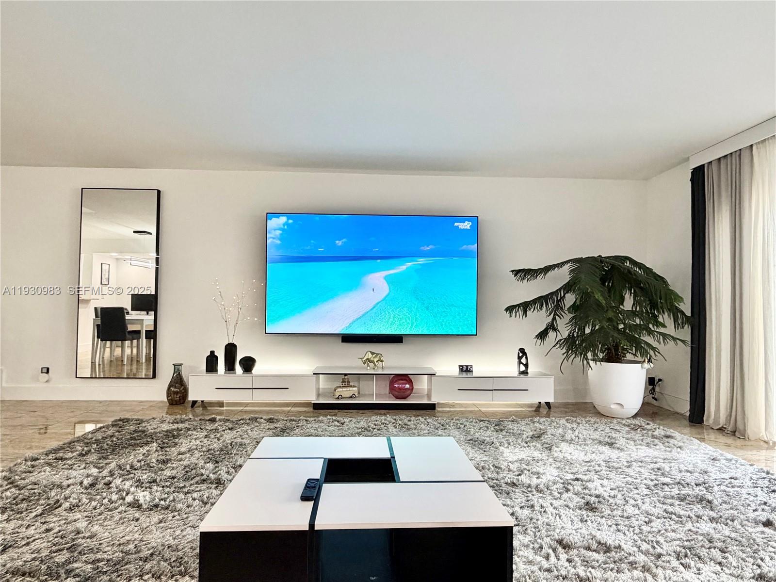 A modern living room features a wall-mounted television, white media console, and a large rug — 934 NE 27th Ave, Hallandale Beach FL 33009, HALLANDALE BEACH, FL