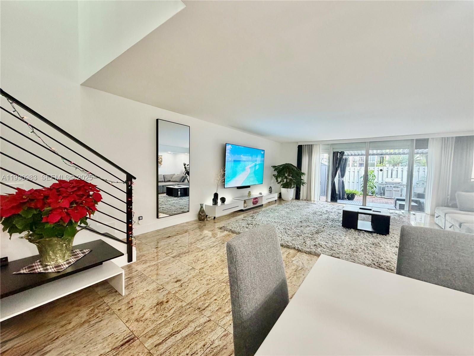 A living room features a staircase, tiled floors, a wall-mounted television, and sliding glass doors — 934 NE 27th Ave, Hallandale Beach FL 33009, HALLANDALE BEACH, FL