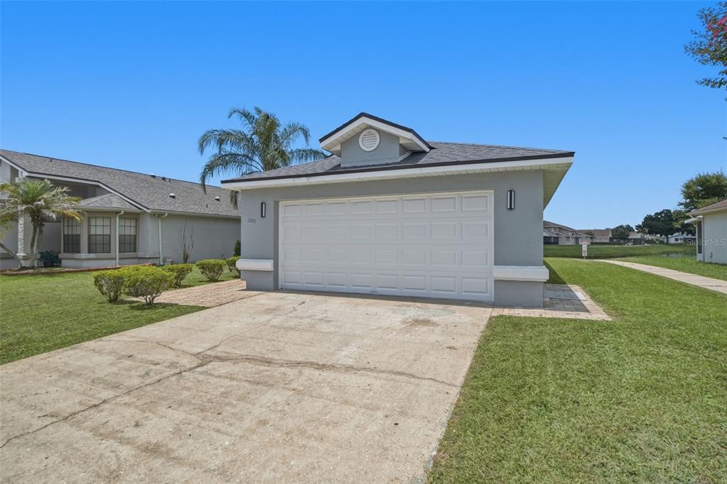 A gray single-story house with a white garage door and a concrete driveway — 1009 WHALEBONE BAY DRIVE, KISSIMMEE, FL