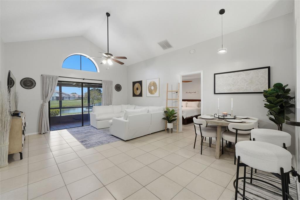 A bright, open-concept living and dining area features vaulted ceilings, tile floors, and water views — 1009 WHALEBONE BAY DRIVE, KISSIMMEE, FL