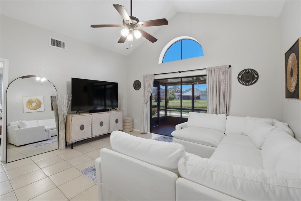 A living room features a white sectional sofa, a television console, and a sliding glass door — 1009 WHALEBONE BAY DRIVE, KISSIMMEE, FL