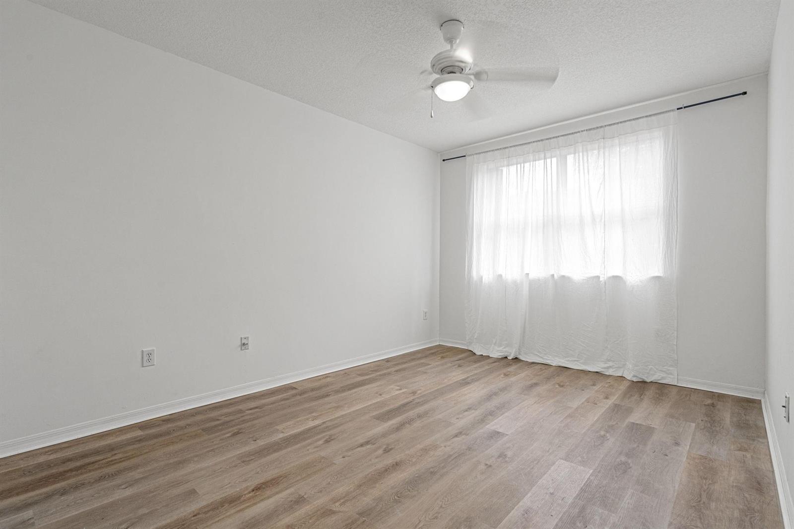 An empty bedroom with white walls, wood-look flooring, a ceiling fan, and a window — 8520 NW 139th Terrace # 1602, Miami Lakes FL 33016, MIAMI LAKES, FL