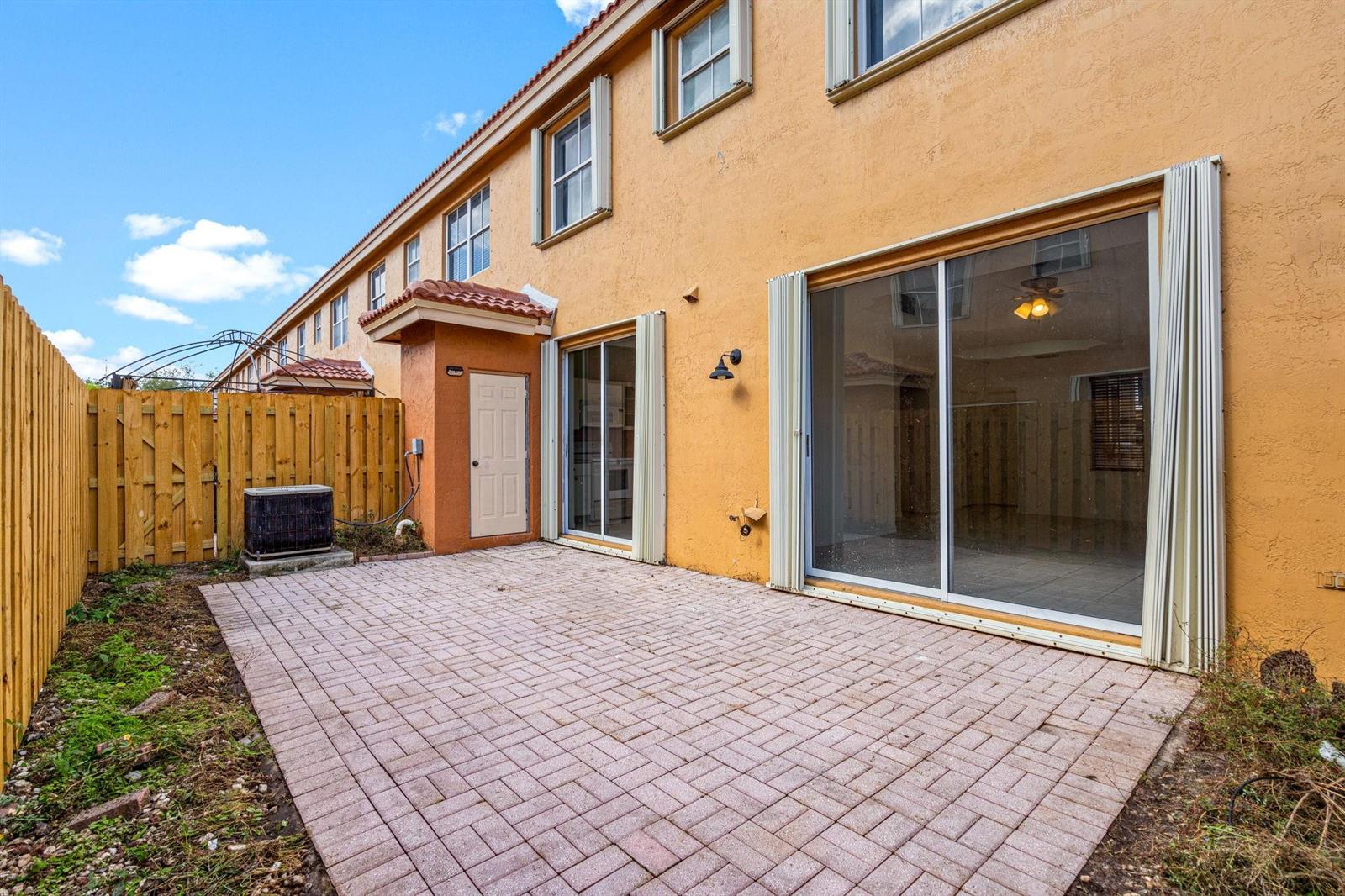 A paved patio sits behind a two-story townhouse with a wooden fence and sliding doors — 8520 NW 139th Terrace # 1602, Miami Lakes FL 33016, MIAMI LAKES, FL