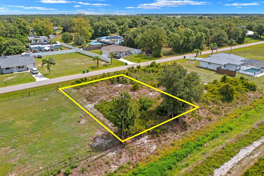 An aerial view shows a vacant, rectangular lot outlined in yellow near a paved road — 29331 LILLIS STREET, PUNTA GORDA, FL